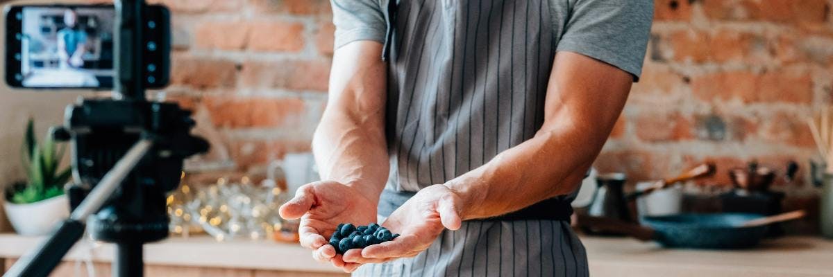 Influencer standing in front of a camera in a kitchen holding blueberries. Micro-influencers tips blog post.